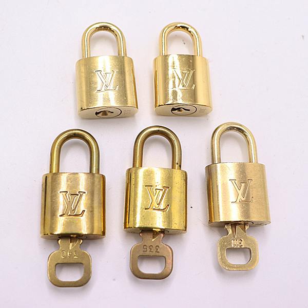 Five gold-tone Louis Vuitton padlocks arranged on a white background, three showing keys inserted.
