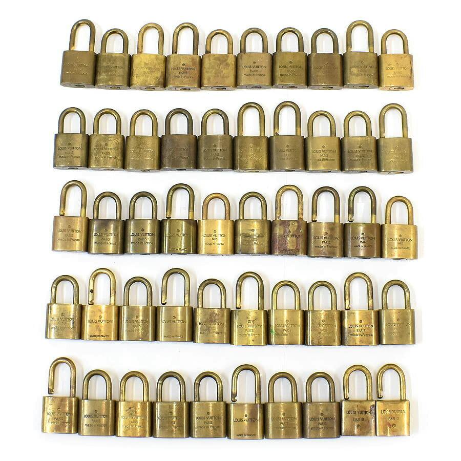 Multiple brass Louis Vuitton padlocks arranged in rows on a white background.