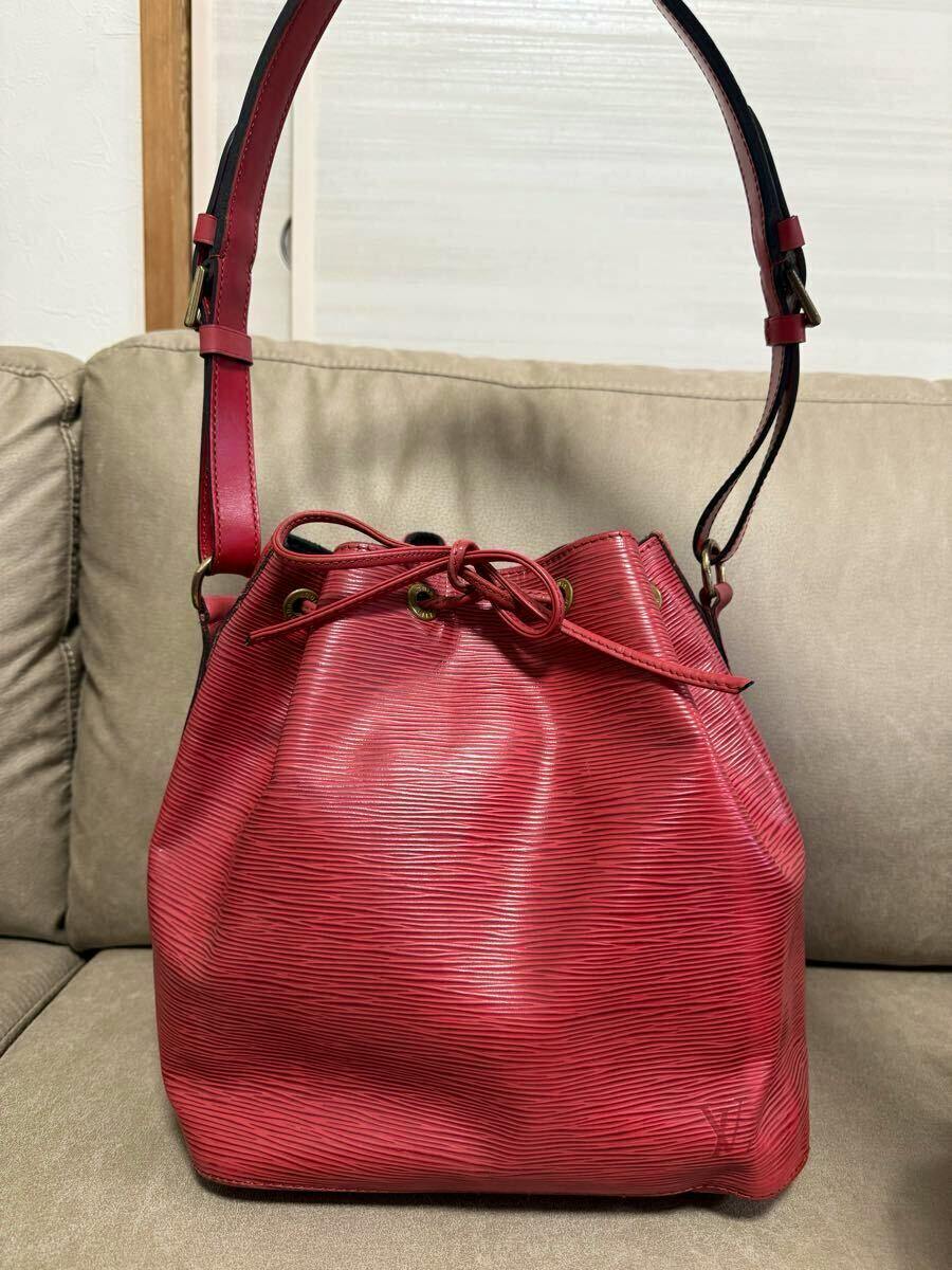 Front view of the red Louis Vuitton Epi Petit Noé shoulder bag placed on a couch.