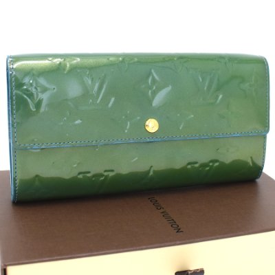 Closed Louis Vuitton Portefeuille Sarah (Vernis enamel) wallet shown resting on a box.