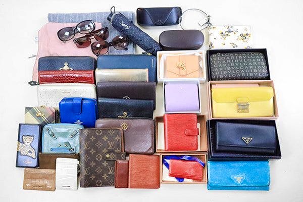 Flat lay of various branded small accessories including wallets, pouches, sunglasses, and scarves on a white background.