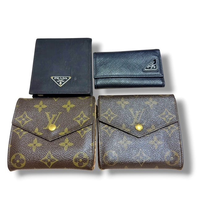 Four wallet/key items on a white background, including two Louis Vuitton monogram fold wallets and two black Prada pieces.