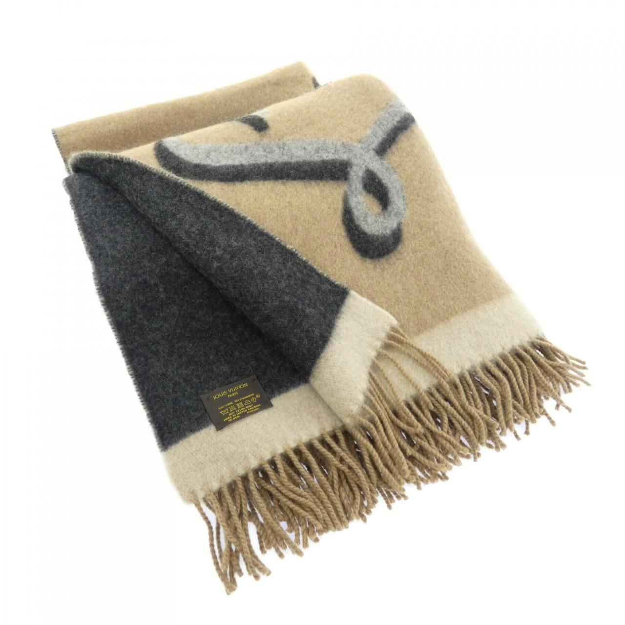 Folded Louis Vuitton cashmere muffler/blanket in beige and gray with fringe and a visible care label.