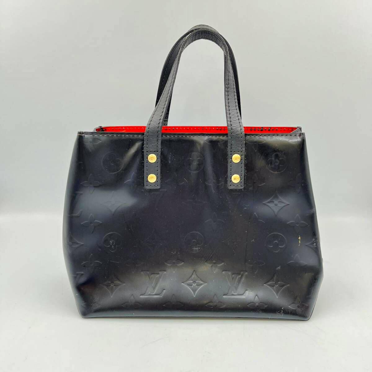 Front view of a black Louis Vuitton Monogram Vernis Lead PM handbag with top handles and red interior visible.