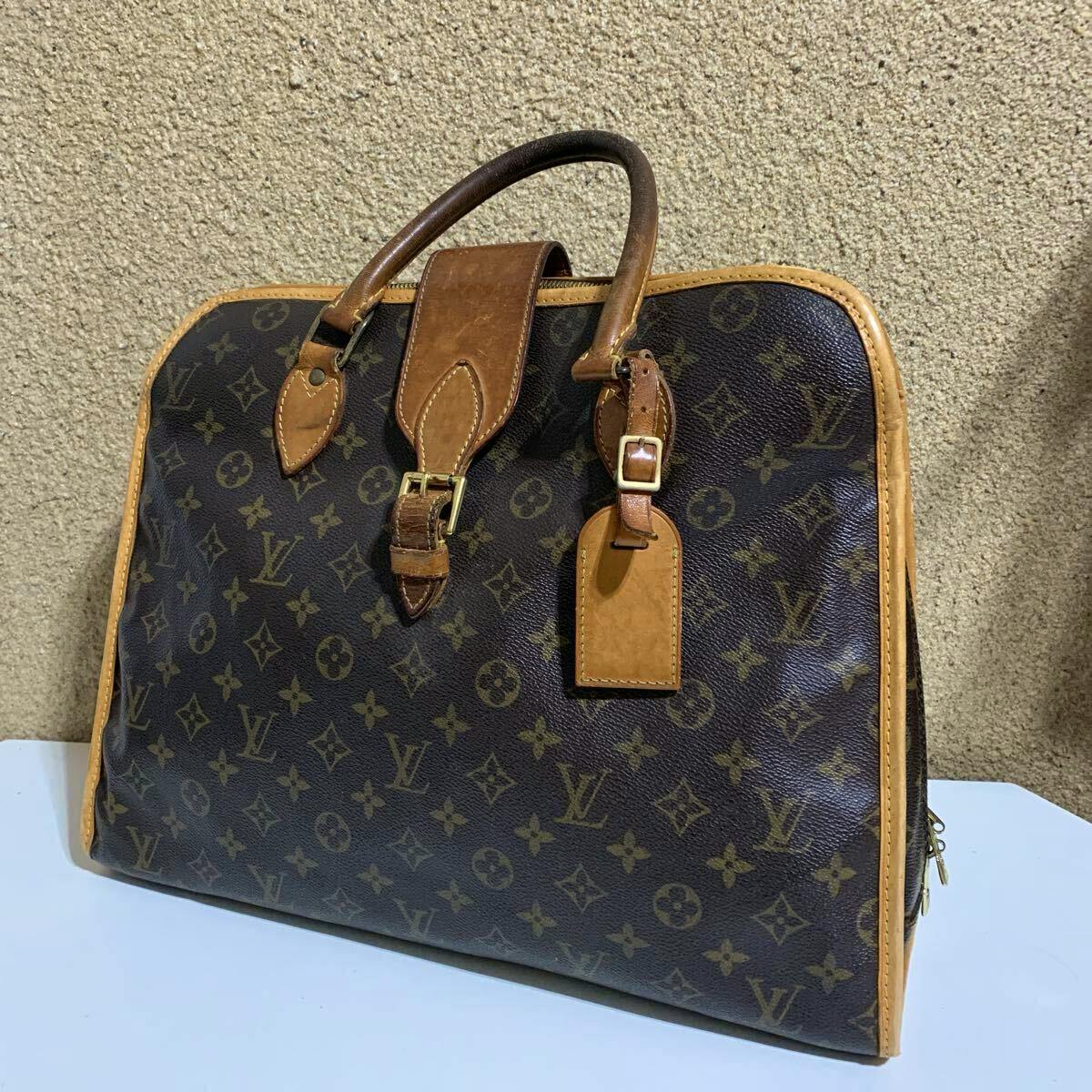 Front view of the LOUIS VUITTON monogram canvas Rivoli business handbag with leather trim, handles, and luggage tag.