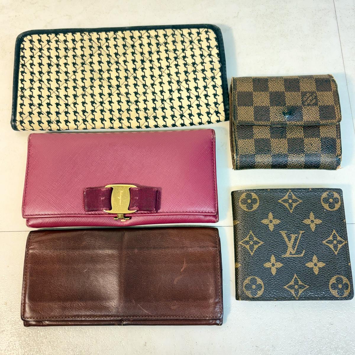 Five wallets arranged on a white surface, including a Louis Vuitton monogram bifold, a Damier check small wallet, a pink long wallet with bow detail, a brown leather wallet, and a patterned white long wallet.
