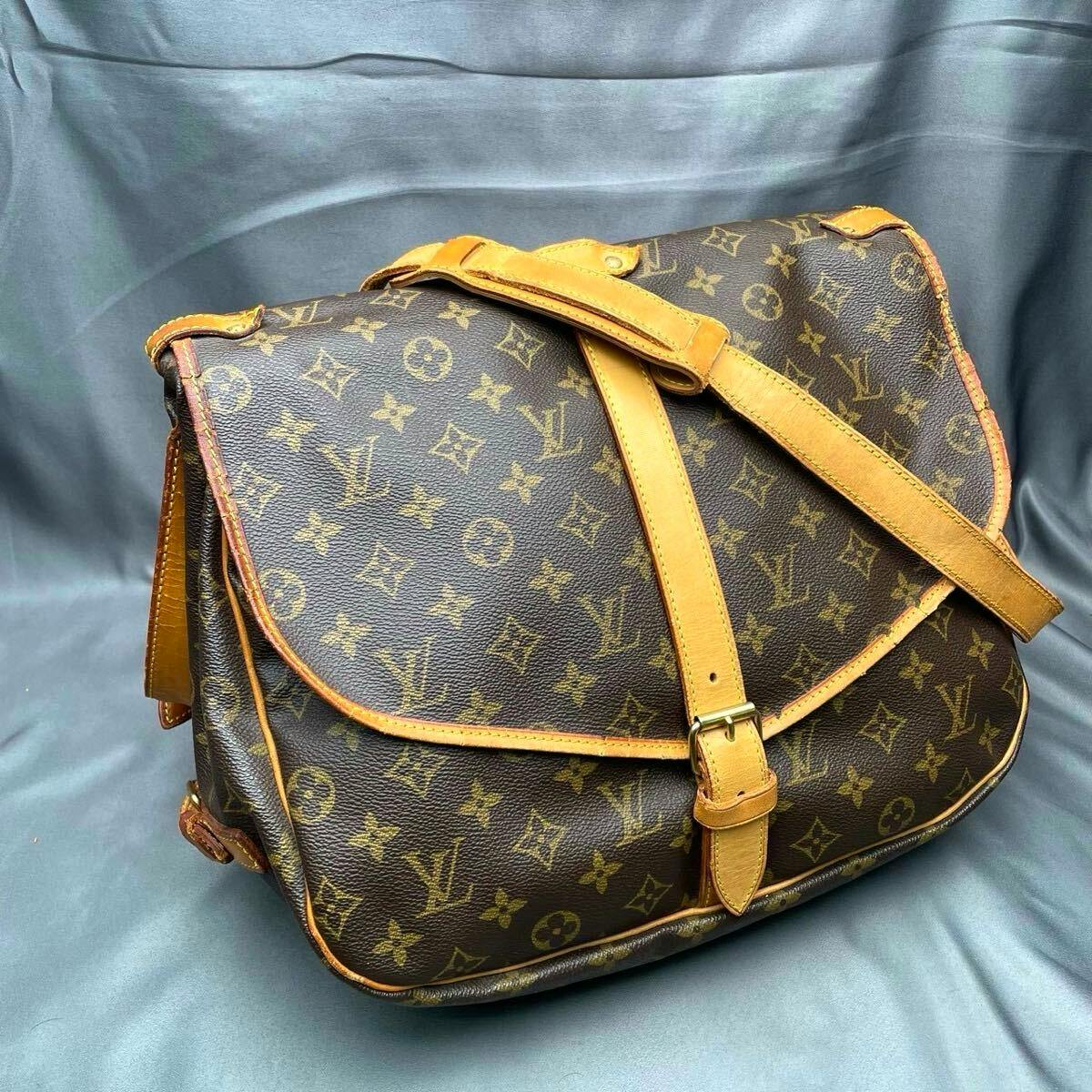 Front angled view of the Louis Vuitton Sommeur 35 monogram shoulder bag with leather strap and buckle on a gray background.