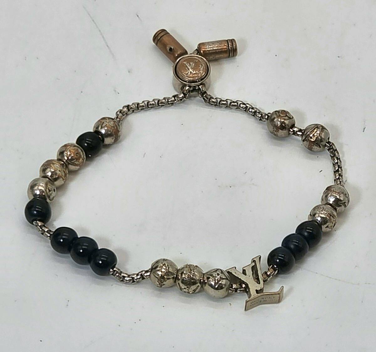 Silver Louis Vuitton bracelet with alternating silver and black beads and an LV charm, laid flat on a white surface.