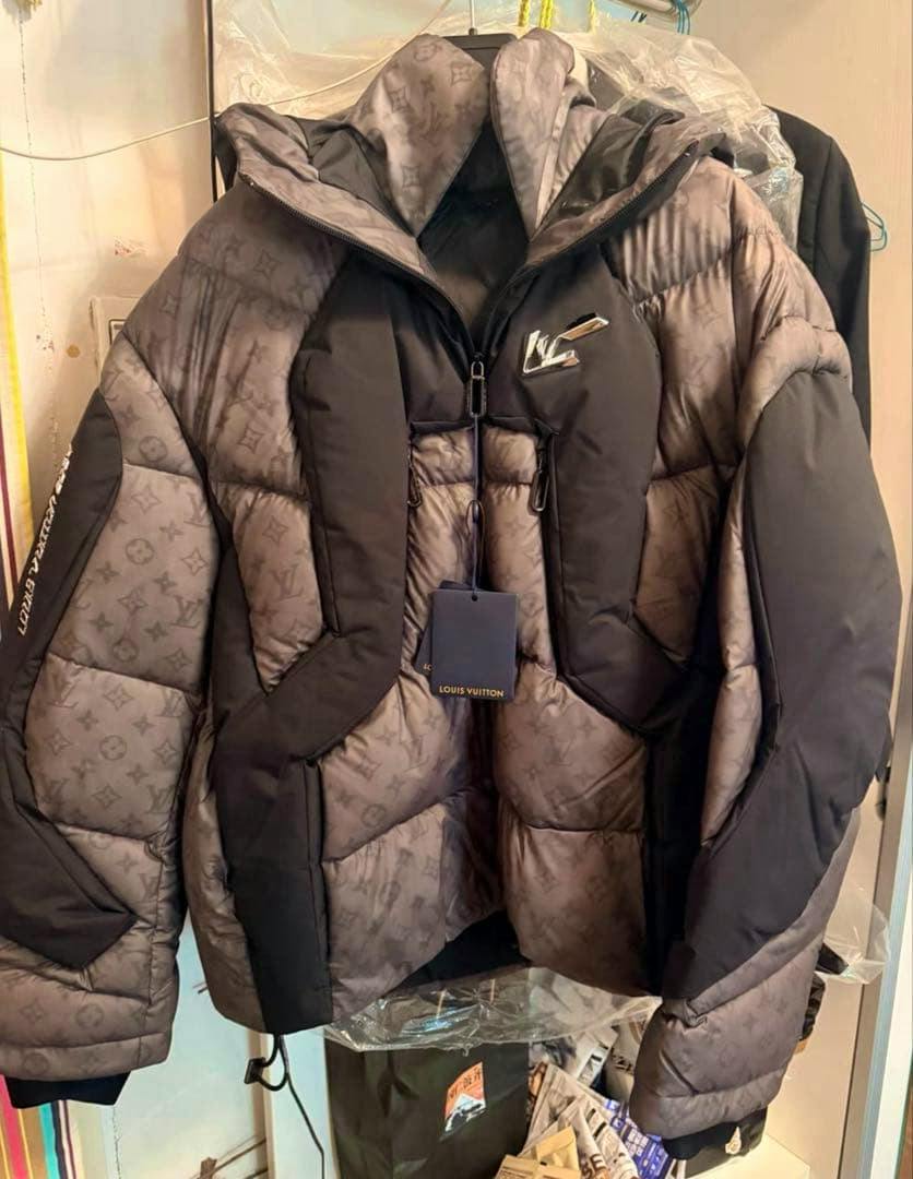Front view of the men's Louis Vuitton monogram puffer down jacket with hood and a hanging Louis Vuitton tag.