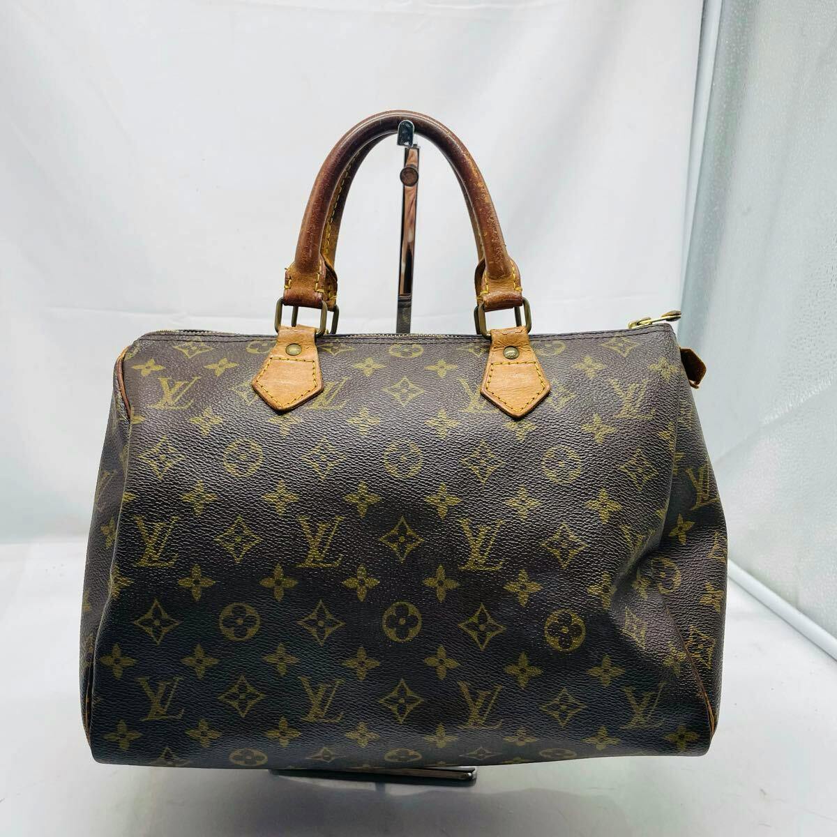 Front view of a brown Louis Vuitton Monogram Speedy 30 vintage canvas handbag with leather handles on a stand.