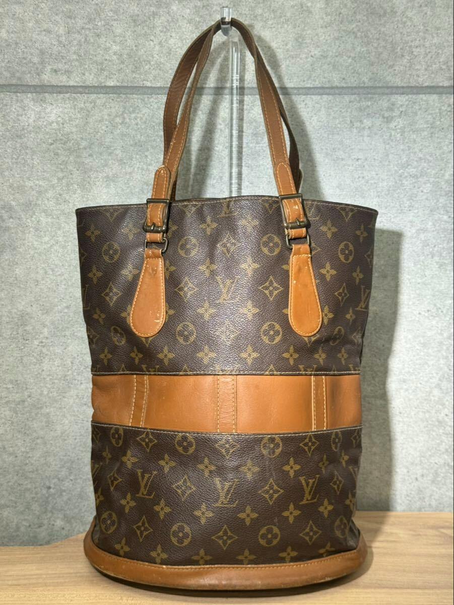 Front view of a brown Louis Vuitton monogram canvas bucket-style tote bag with leather trim and shoulder straps.