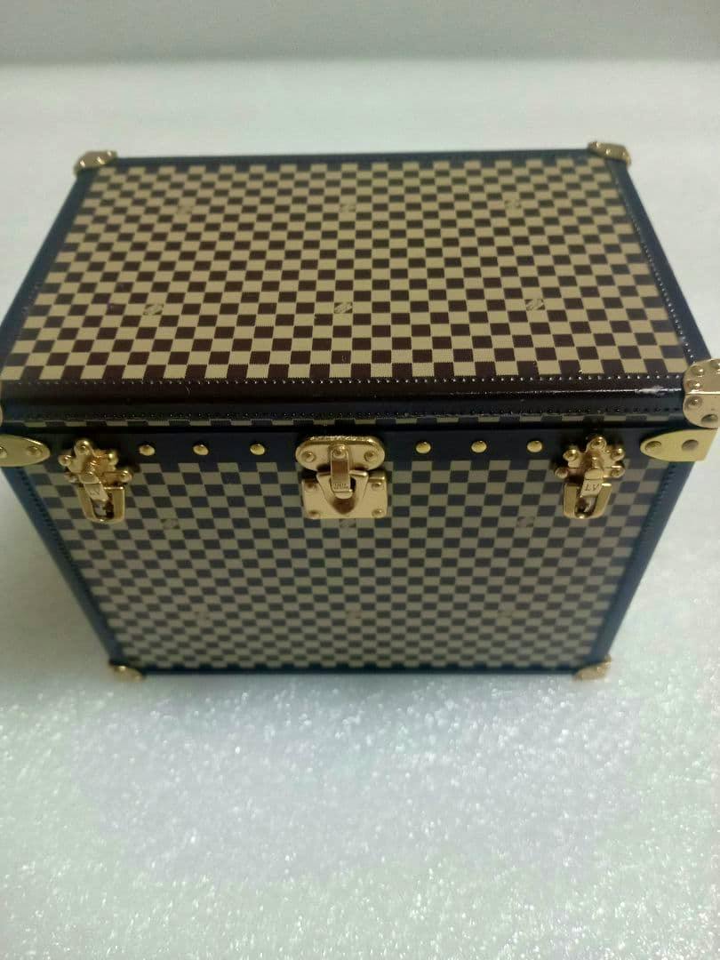 Angled top-front view of a wooden trunk-style small box with a checkered pattern and gold-tone latches.