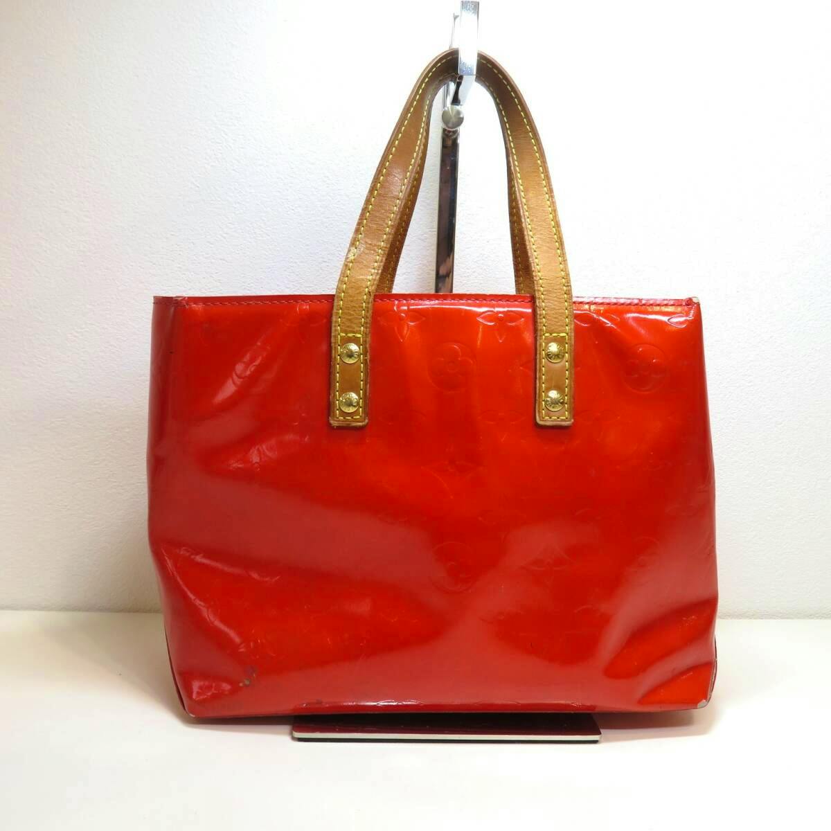 Front view of the red LOUIS VUITTON ヴェルニ リードPM bag with brown handles displayed on a stand.