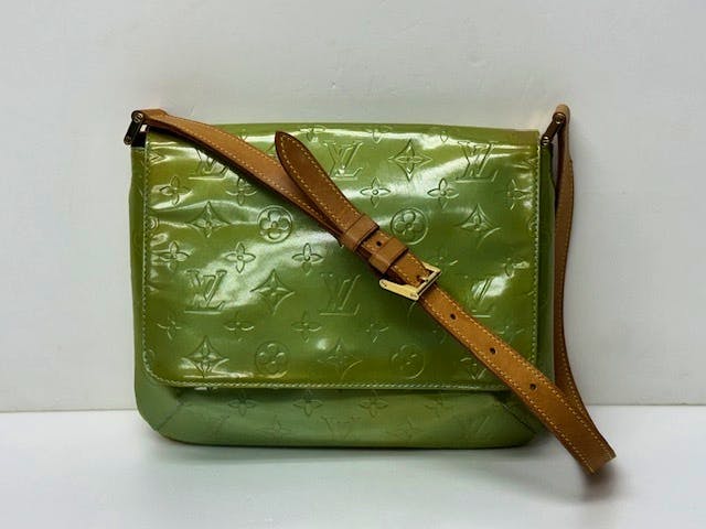 A green Louis Vuitton Vernis patent leather Thompson shoulder bag with embossed monogram and a tan adjustable shoulder strap against a white background.