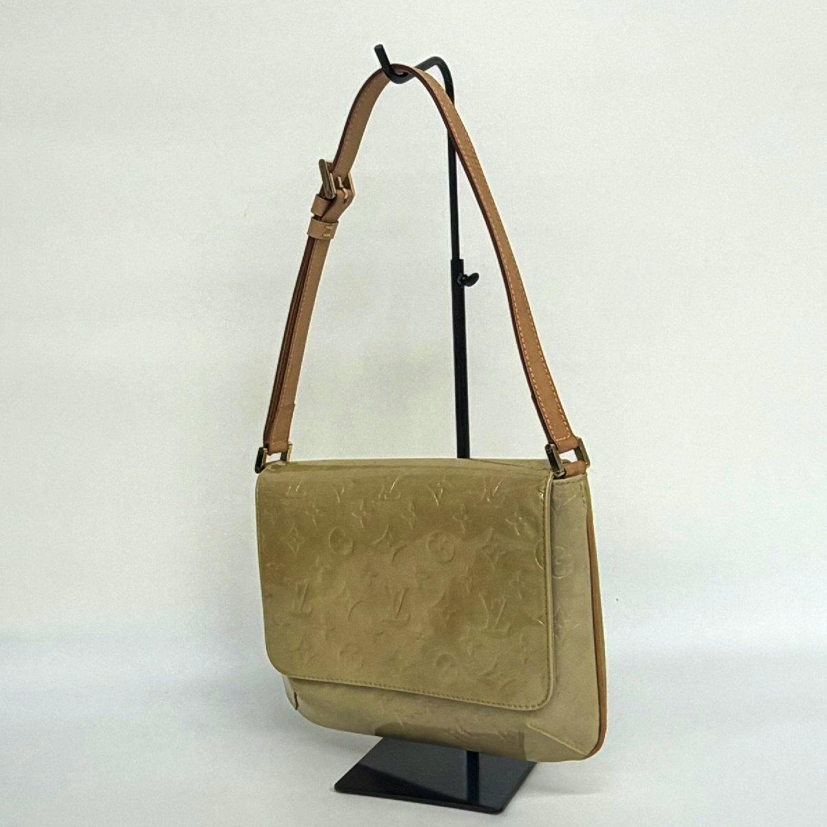 Yellow Louis Vuitton shoulder bag (Vernis Thompson Street) shown hanging on a display stand, front and strap visible.