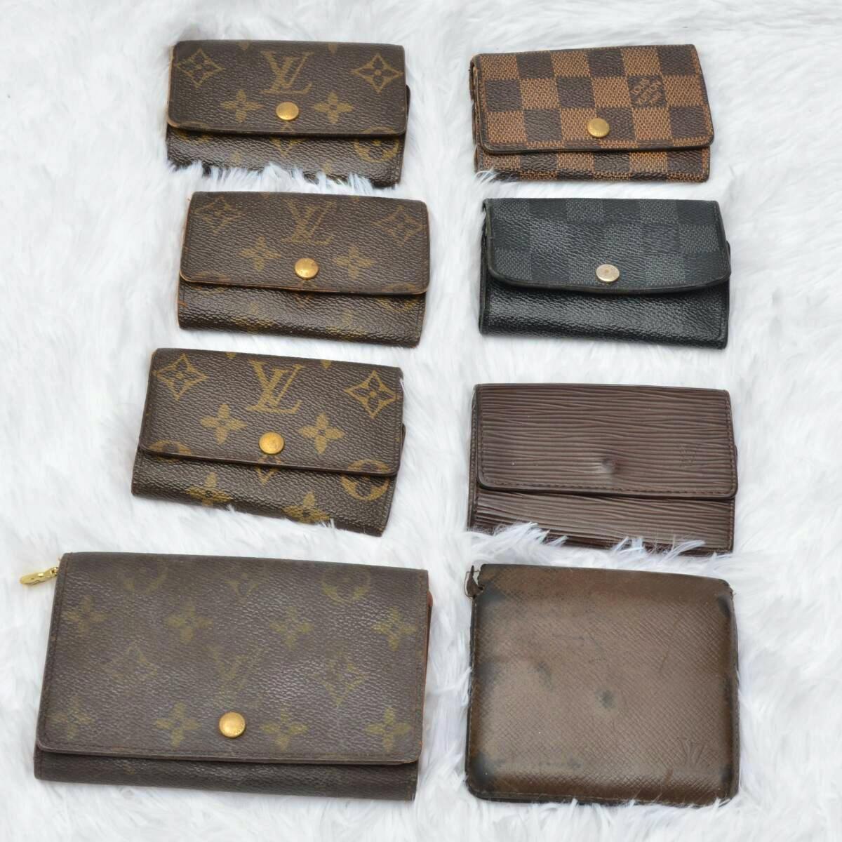 Eight LOUIS VUITTON wallets and key cases arranged on a white fur background.