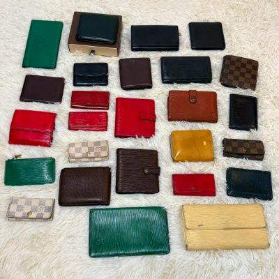 Several wallets and key cases in various colors and Louis Vuitton Damier and Epi patterns laid out on a light rug.