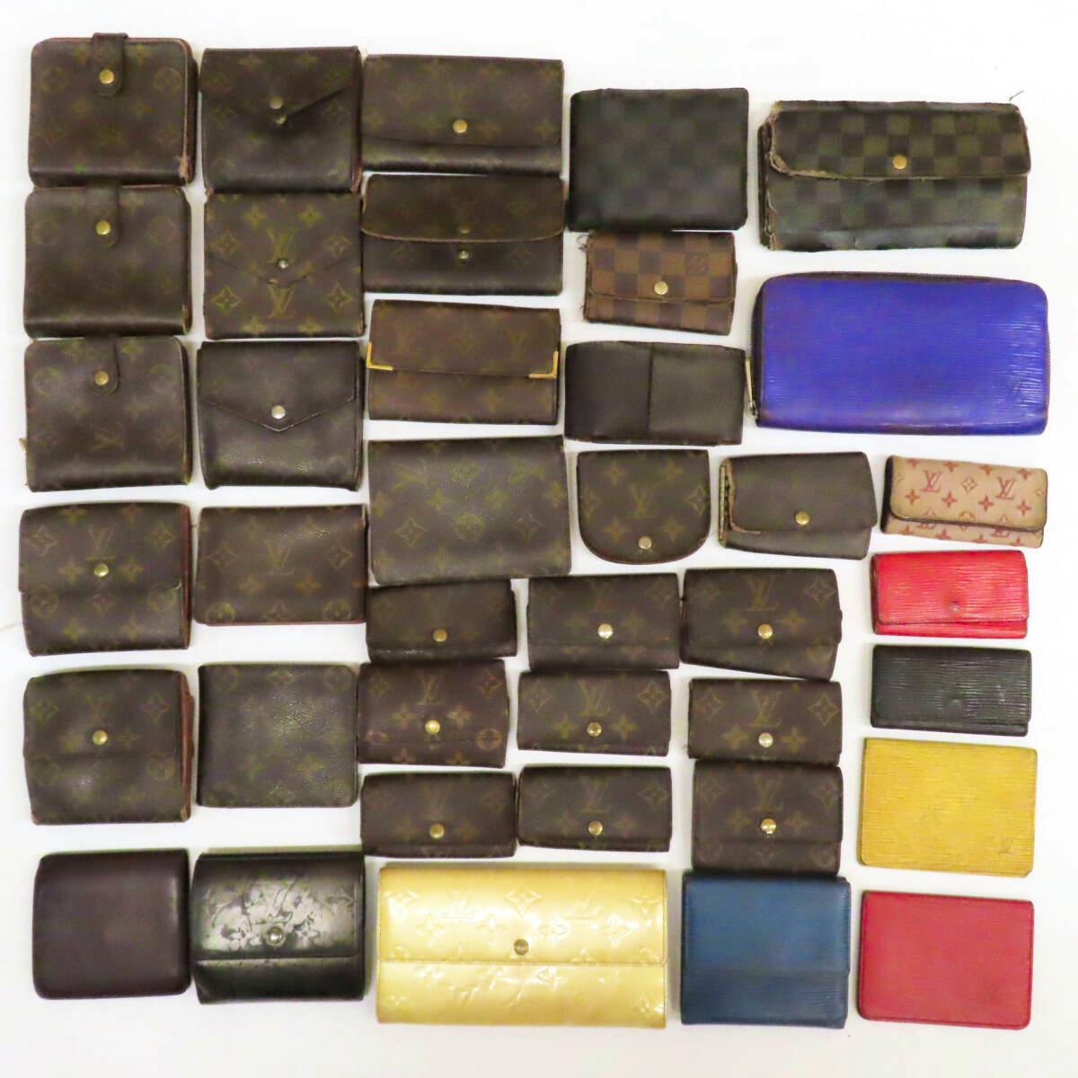 Array of many Louis Vuitton small wallets, card cases, and key cases in monogram, Damier, Epi, and Vernis finishes arranged on a white background.