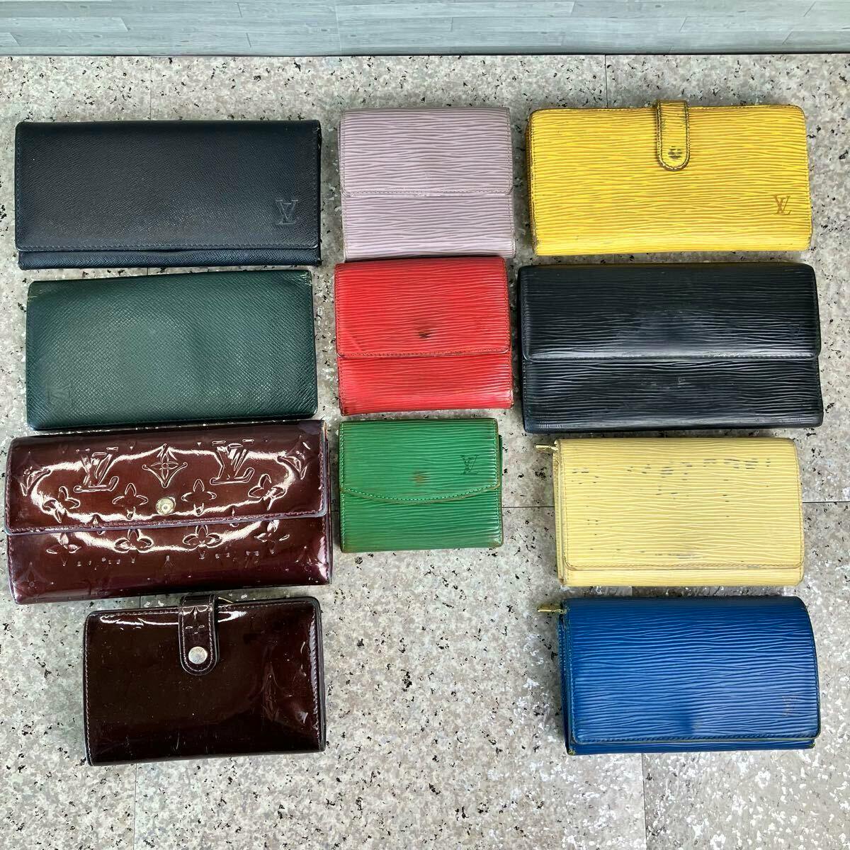 Eleven Louis Vuitton wallets and small leather goods in various colors and leathers arranged on a tiled floor.