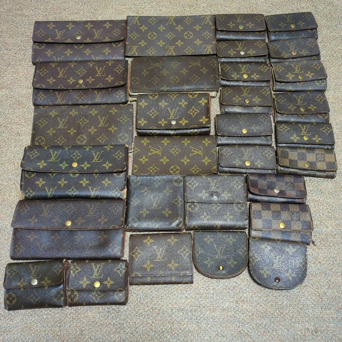 Multiple Louis Vuitton wallets and small pouches in monogram and Damier patterns arranged on a carpeted floor.