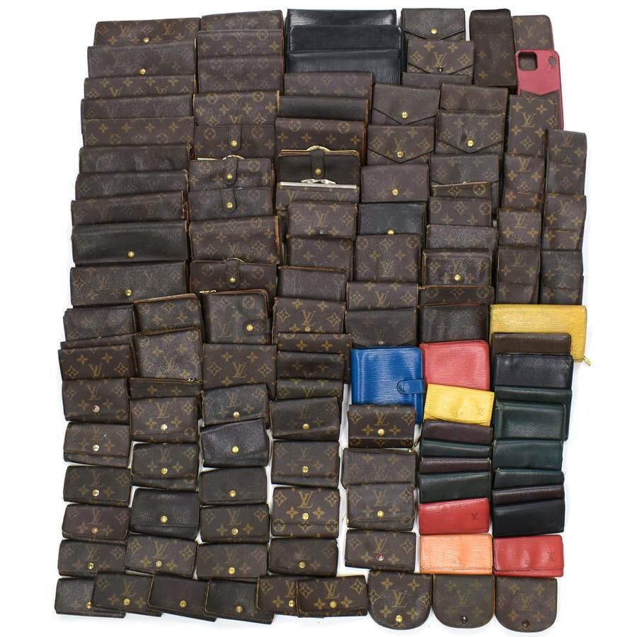 Lot of Louis Vuitton wallets and small leather goods, mostly monogram canvas with some colored pieces, arranged flat on a white background.