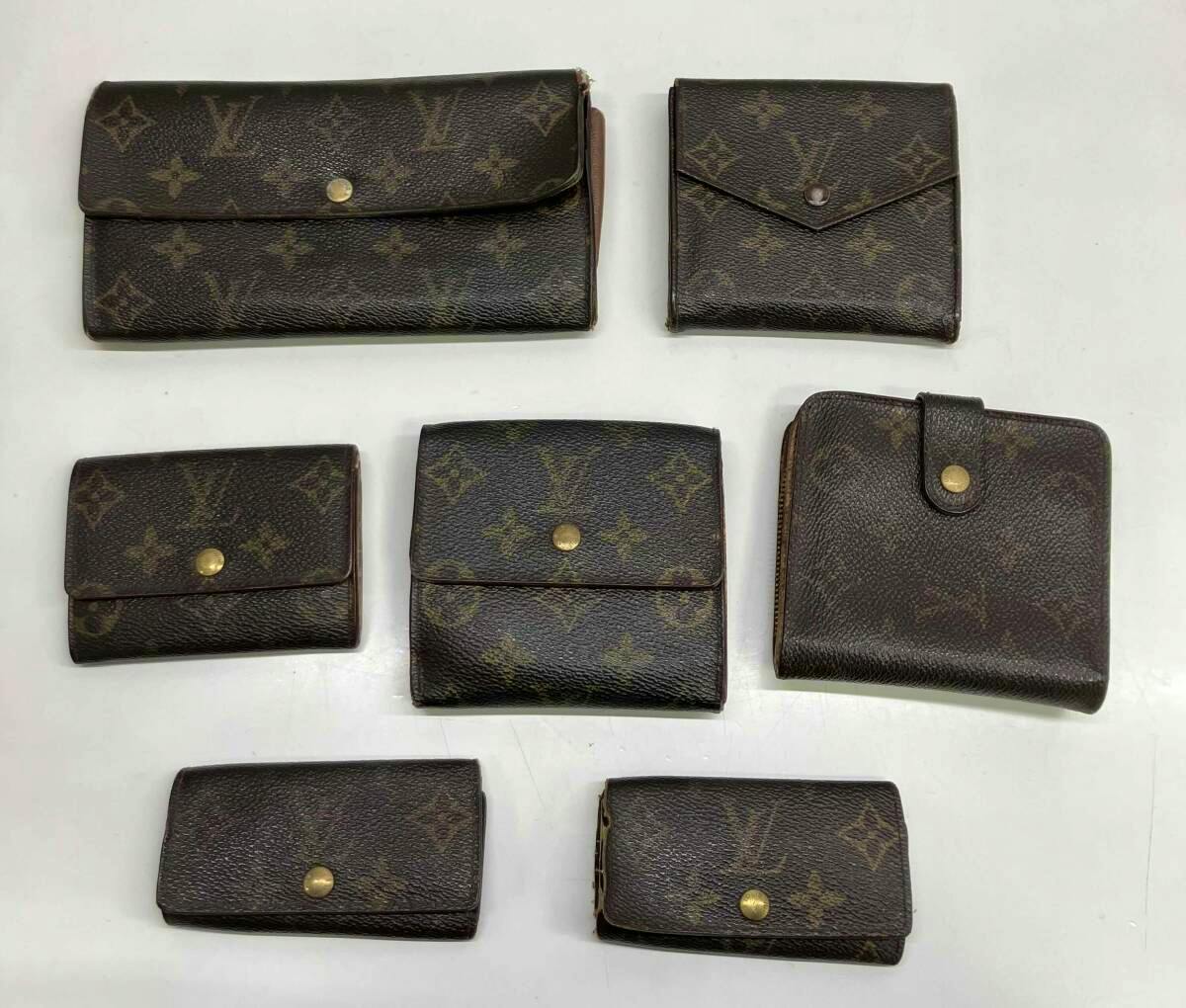 Seven Louis Vuitton monogram wallets and small leather goods arranged on a white surface.
