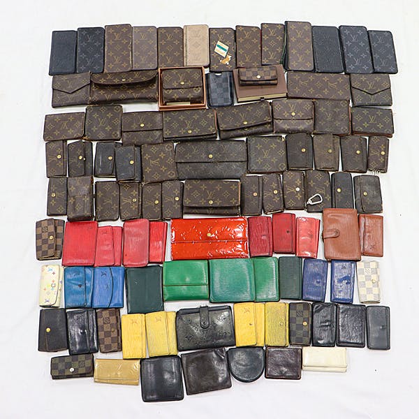 Overhead photo of many wallets and small leather goods arranged on a white background, including several Louis Vuitton monogram pieces.