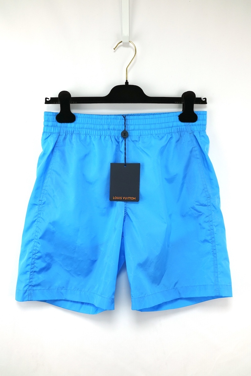 Blue Louis Vuitton men's board shorts hanging on a hanger with a visible tag.