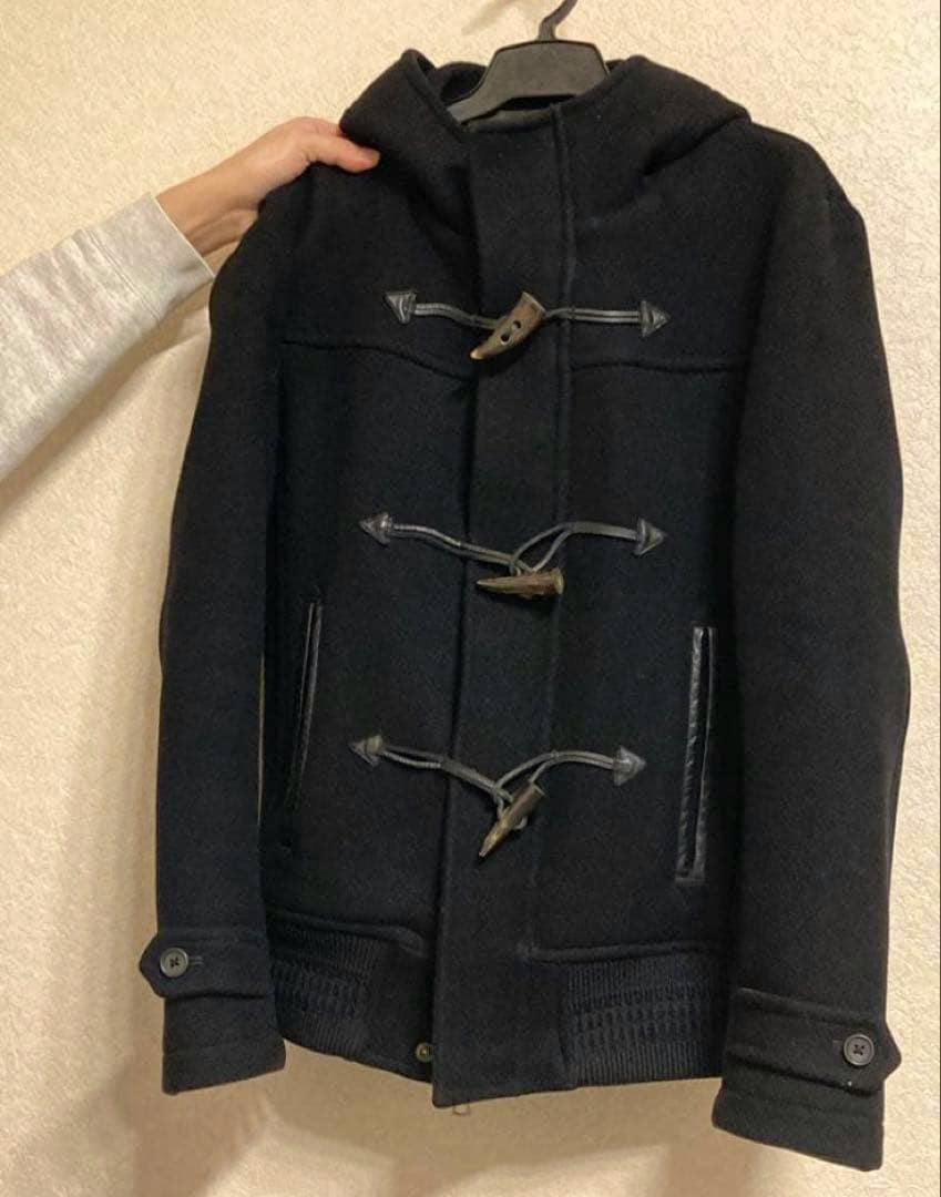 Front view of a dark wool men's duffle coat with three wooden toggle closures and a hood hanging on a hanger.