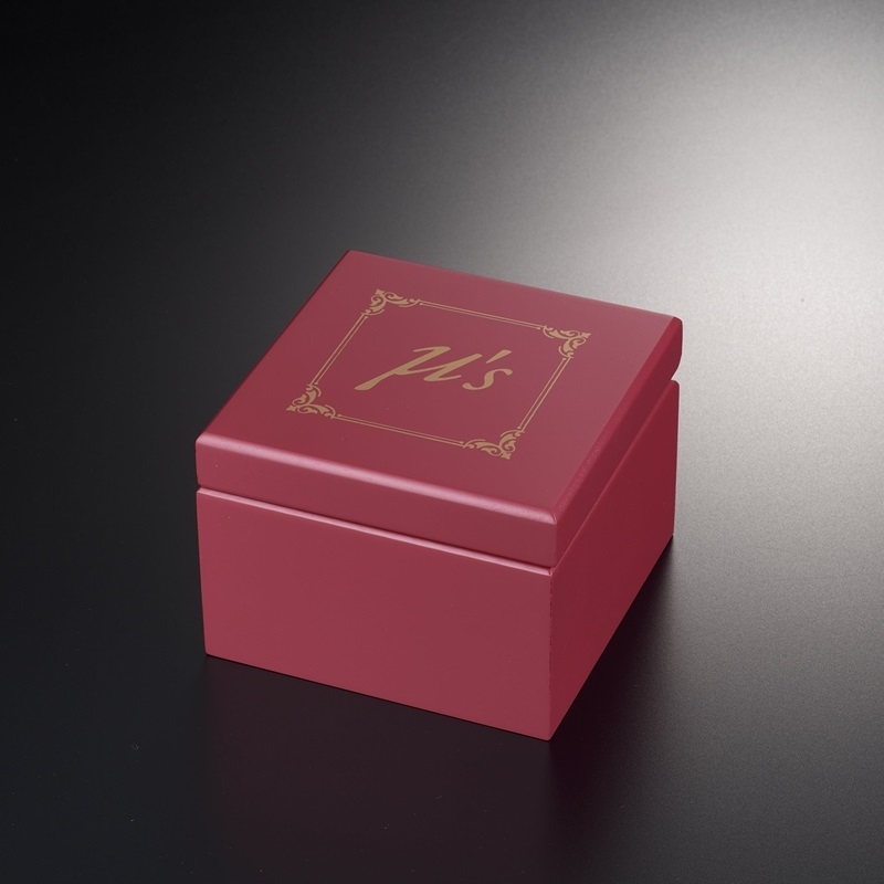 Closed red square music box with a gold decorative emblem on the lid, photographed on a dark surface.