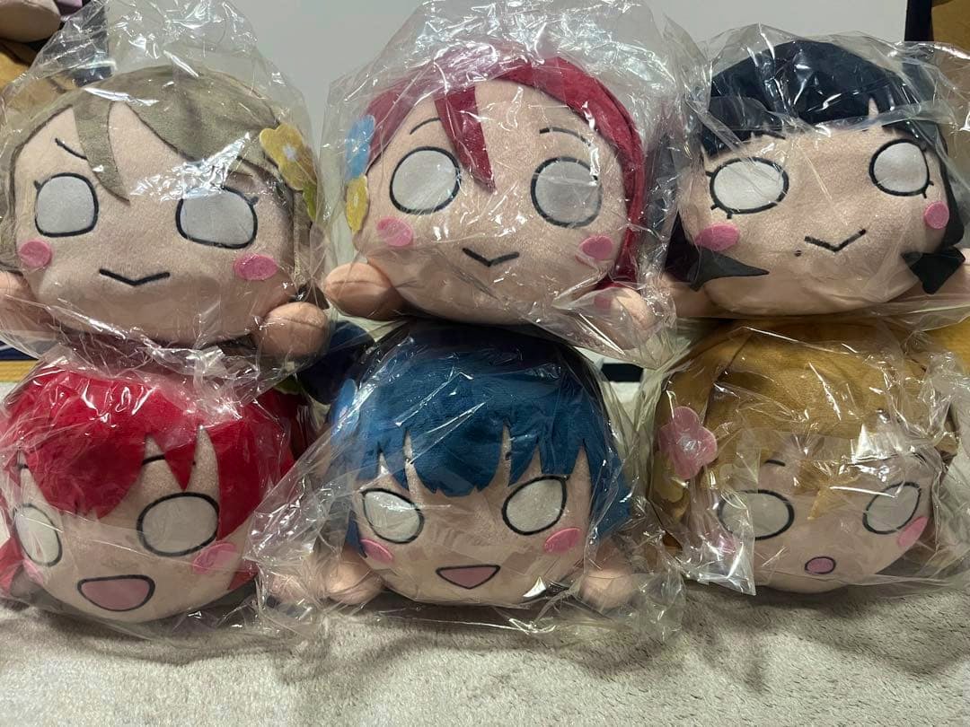 Six Love Live! School Idol Festival ALL STARS nesoberi plush heads wrapped in plastic, arranged in two rows on a surface.