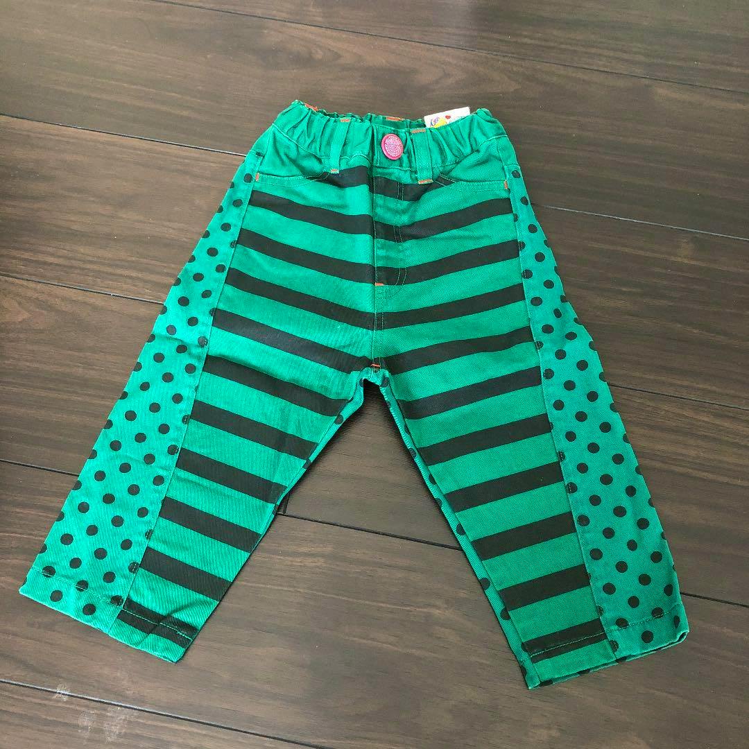 Front view of green children's cotton pants (size 90) with black horizontal stripes and polka-dot side panels laid flat on a wood floor.