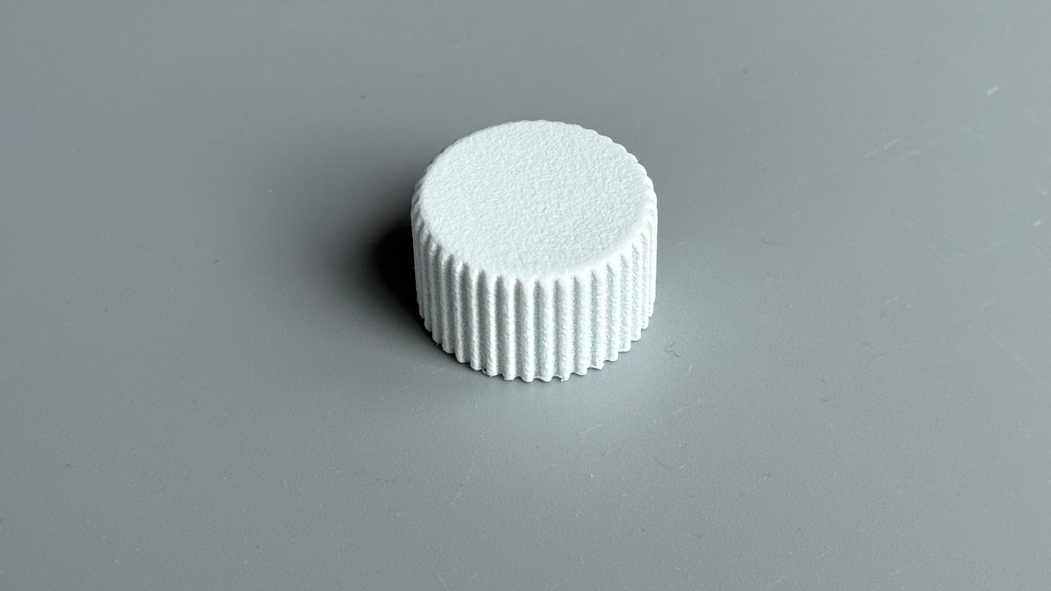 A low-profile white rotary encoder knob photographed on a gray background.