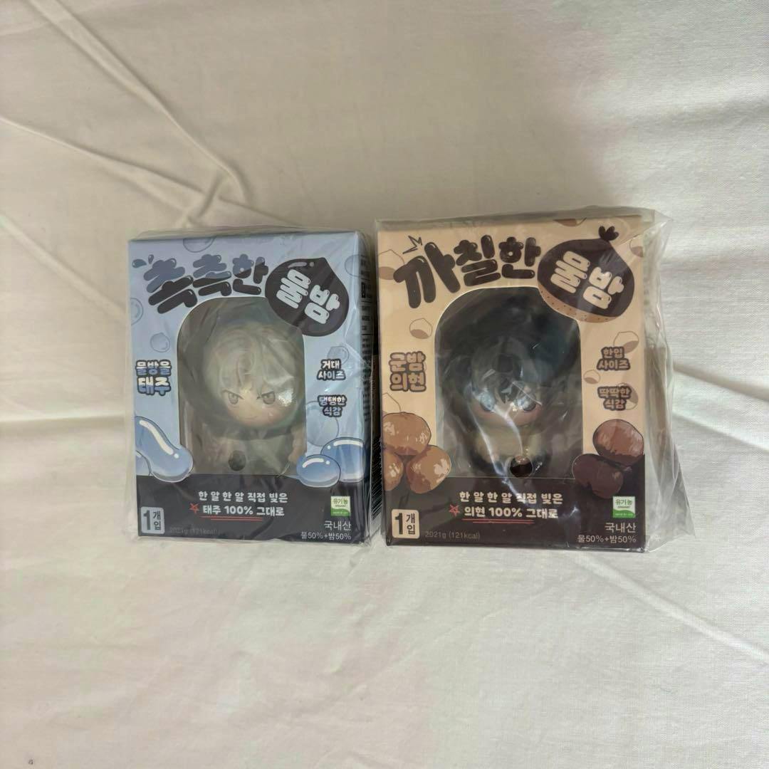 Front view of two boxed Korean BL "水辺の夜" mini figure packages (blue and beige) showing the figures through front windows on a plain fabric background.