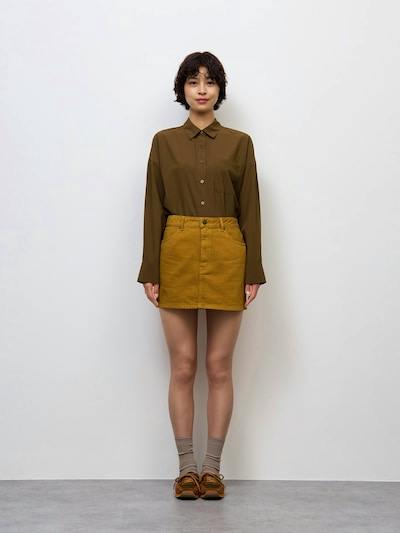 Front view of a model wearing the low-waist corduroy mini skirt with a tucked-in brown shirt, socks, and shoes.