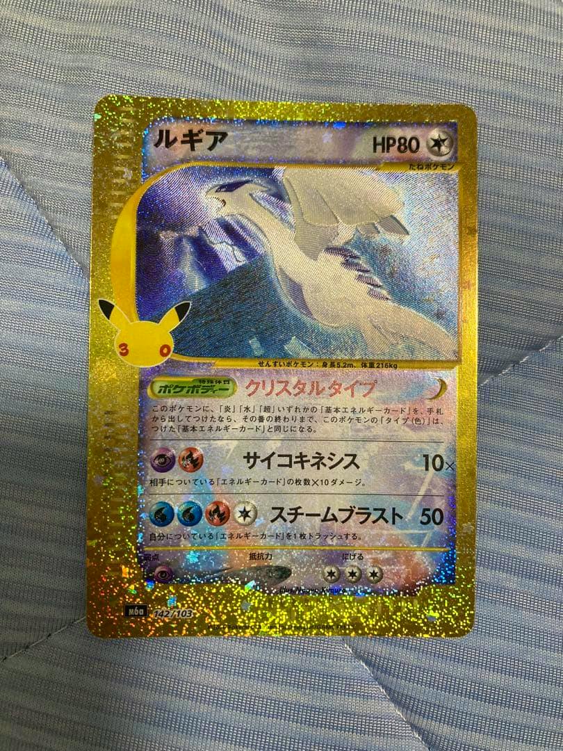 Front of the Lugia 30th anniversary crystal trading card showing Lugia artwork and a holographic gold border on a fabric background.