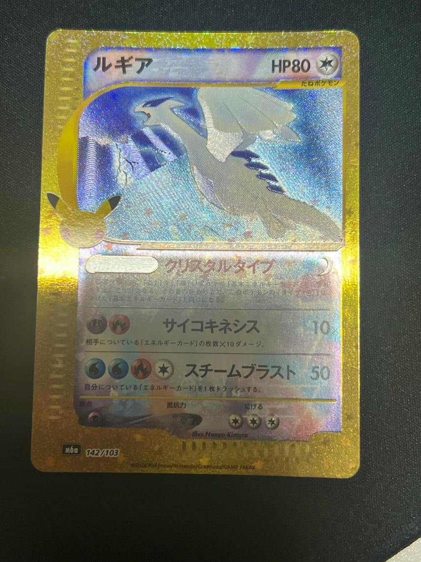 Holographic Lugia Pokémon trading card (M6a 142/103, 30th CELEBRATION) photographed on a dark surface showing the full front of the card.