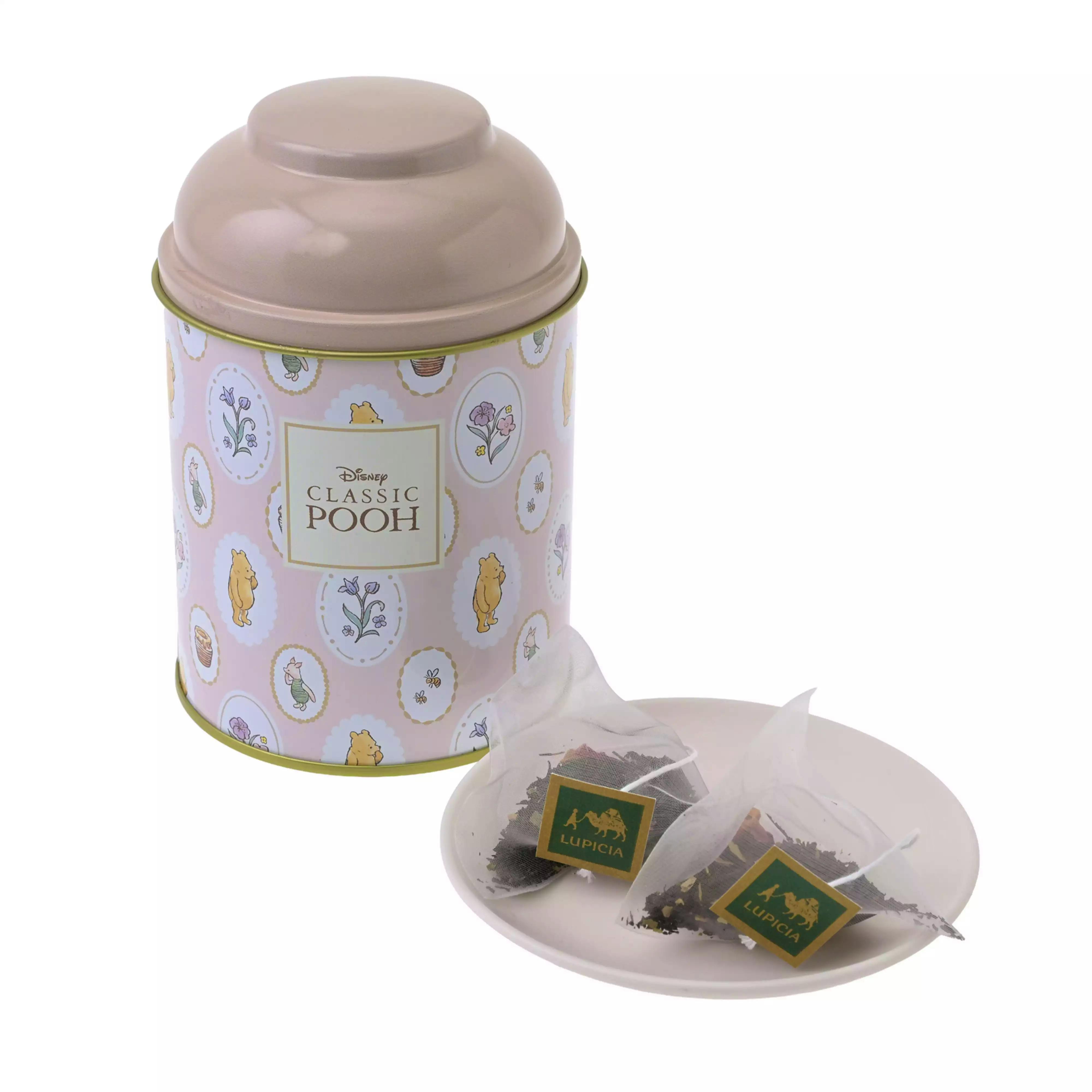 A decorative LUPICIA "Classic Pooh" tea tin shown with LUPICIA pyramid black tea bags on a small white dish.