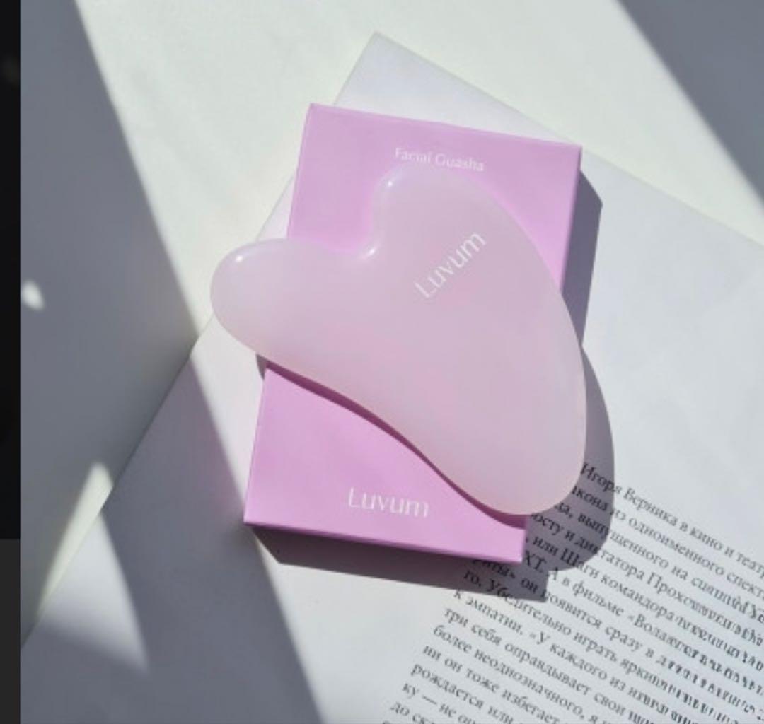 Pink Luvum facial gua sha stone resting on its pink box on a sheet of paper.