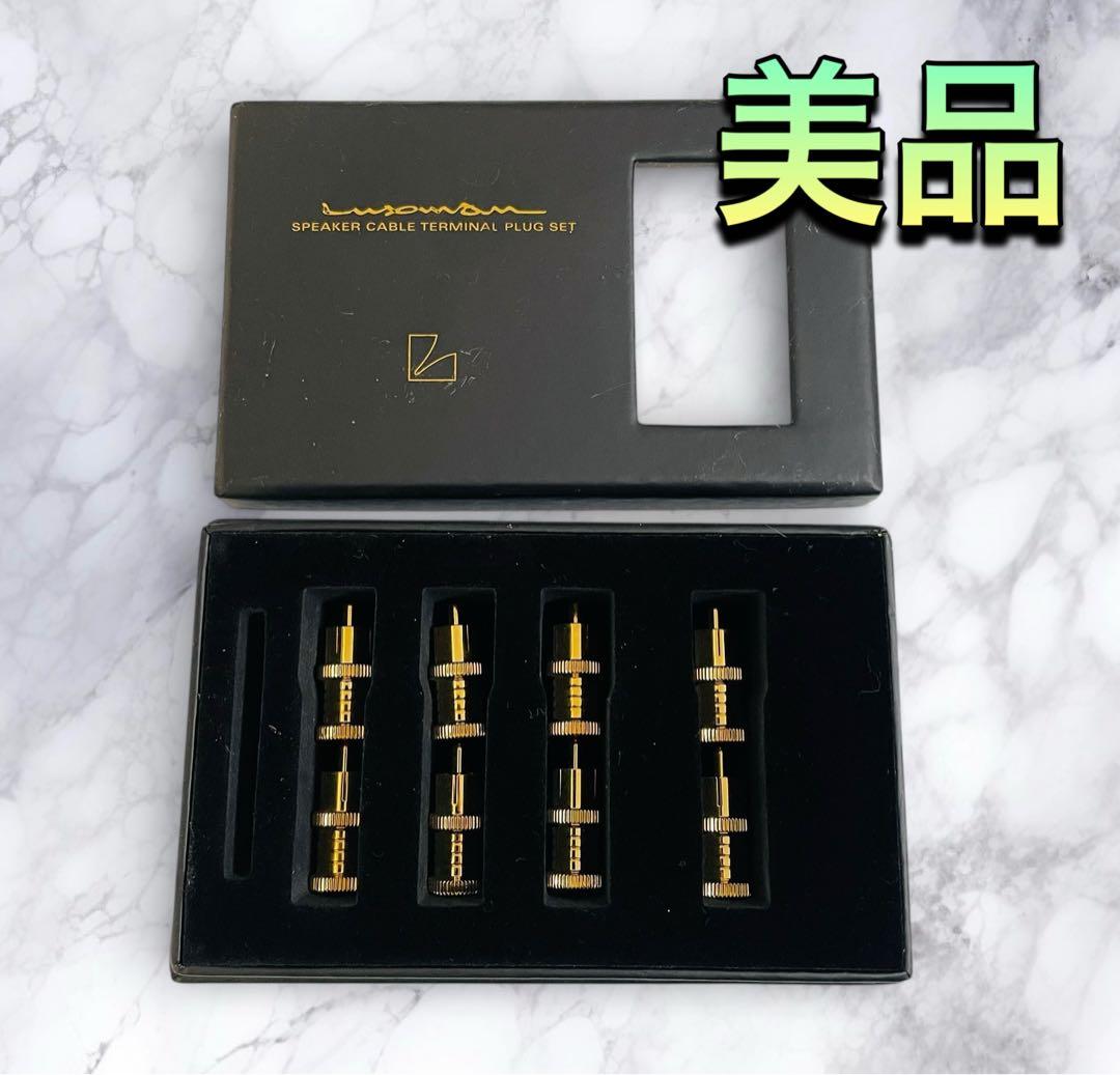 Open black Luxman speaker cable terminal box showing five gold RCA short-pin plugs arranged in a foam insert.