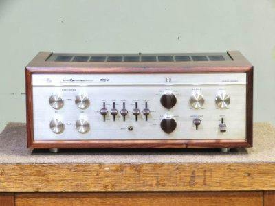 Front view of a silver-front stereo amplifier with wooden side panels sitting on a wooden surface.