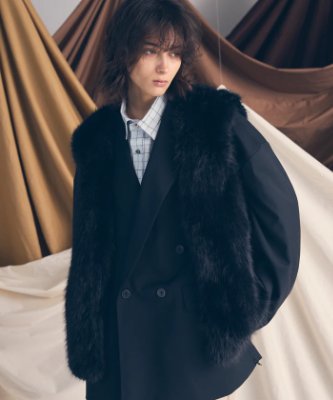 Model wearing the dark eco-fur vest layered over a double-breasted blazer against a draped fabric background.