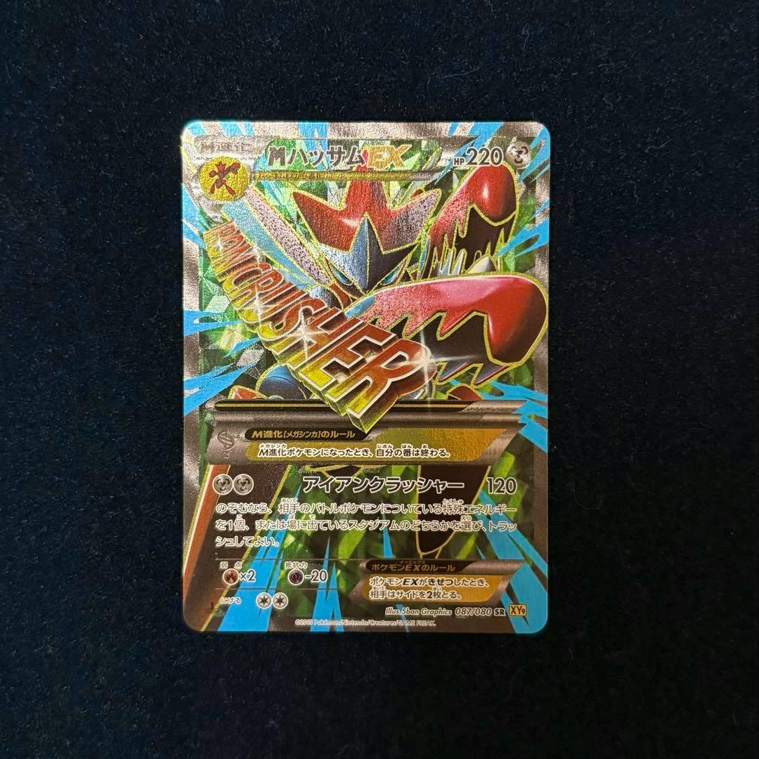 Photograph of the MハッサムEX SR XY9 trading card (front) showing the full holographic card artwork and text on a dark textured background.