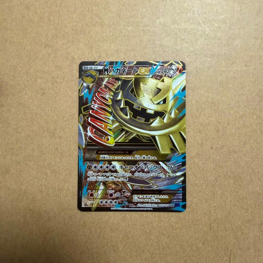 Full photo of the trading card 爆熱の闘士 mハガネールEX SR placed on a brown cardboard background.