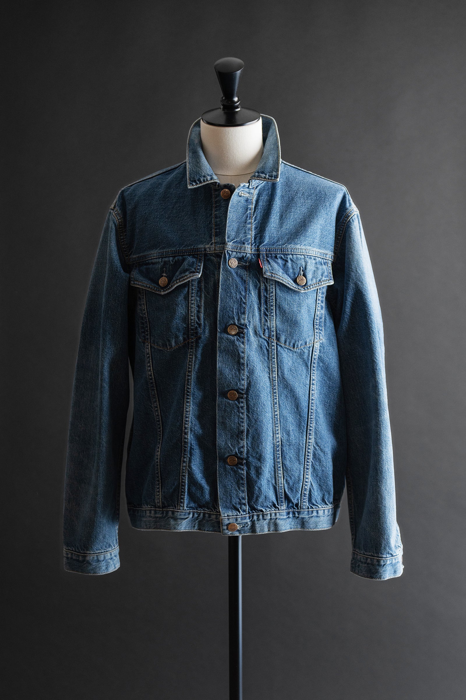 Front view of a blue denim tracker jacket displayed on a mannequin against a dark background.