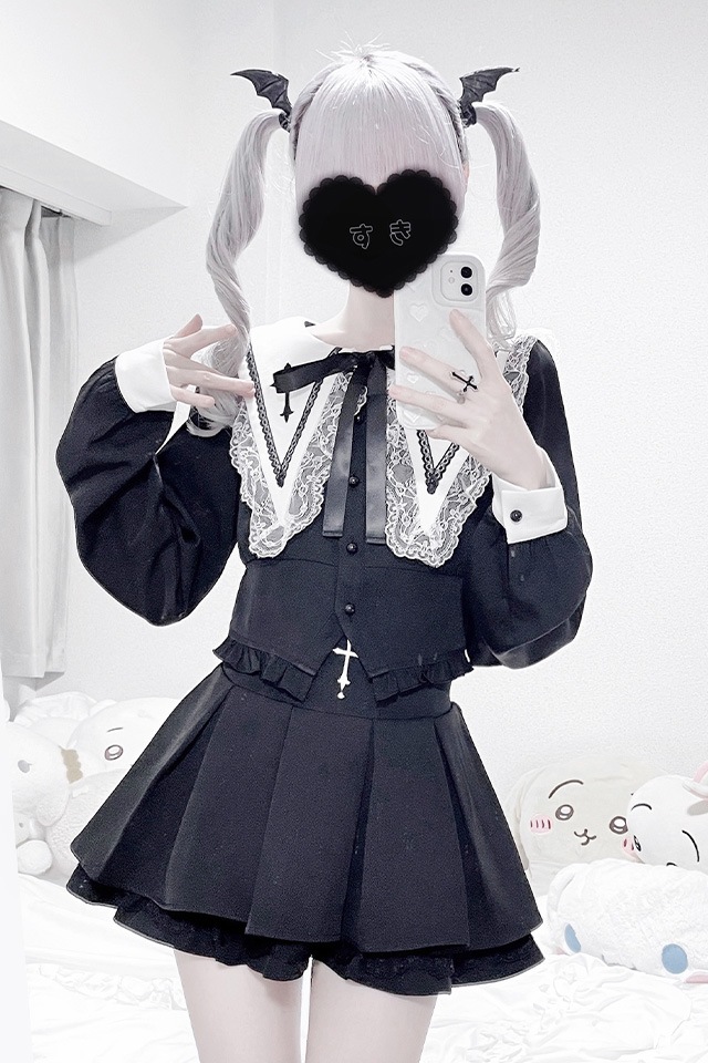 Mirror selfie of a person wearing the black two-piece short-length suit with lace collar, cross embroidery, pleated skirt, and ribbon bow; face obscured.