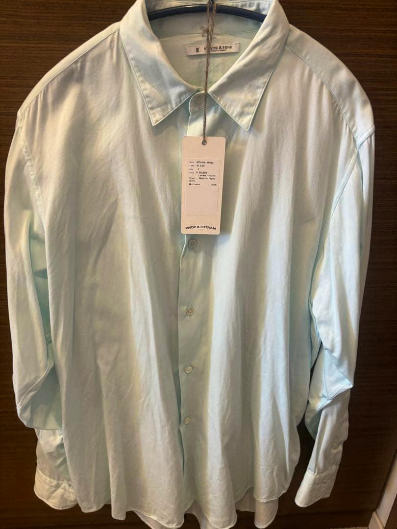 Light blue men's cotton button-up shirt hanging on a hanger with its tag visible.