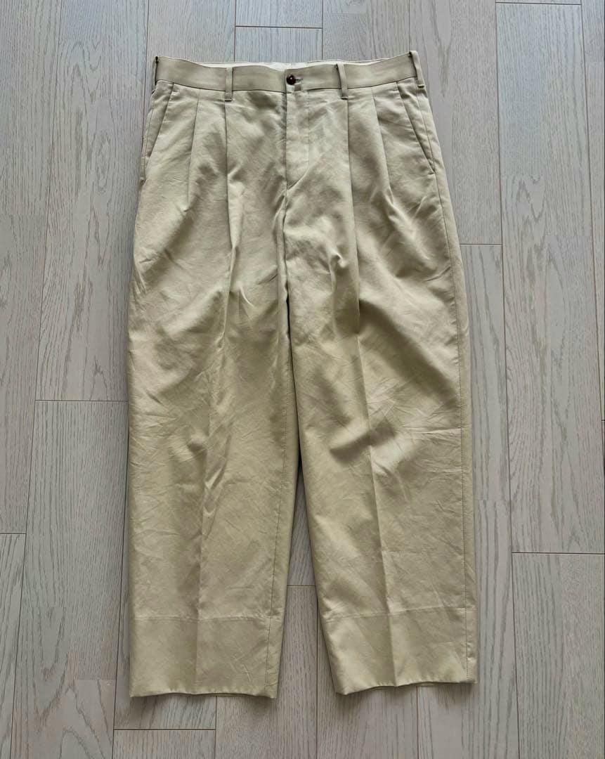 Flat-lay front view of beige men's chinos (cotton pants) laid flat on a light wood floor.