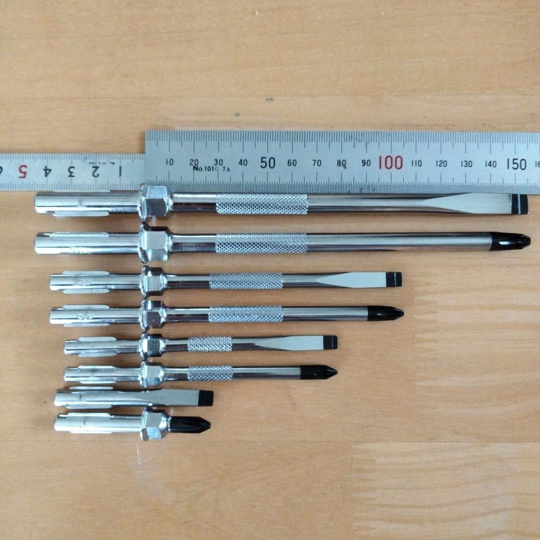 Eight screwdriver blades laid side-by-side on a wooden surface with a ruler above them showing their lengths.