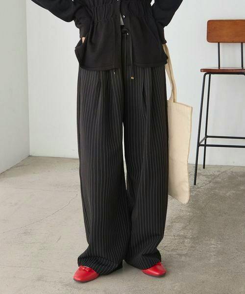 Model wearing black pinstripe wide-leg slacks pants shown full length with red flats and a tote bag.